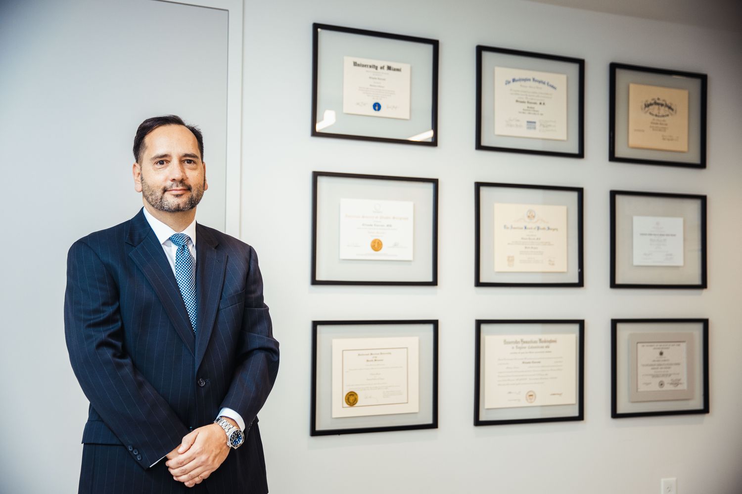 Person in suit standing beside framed diplomas.