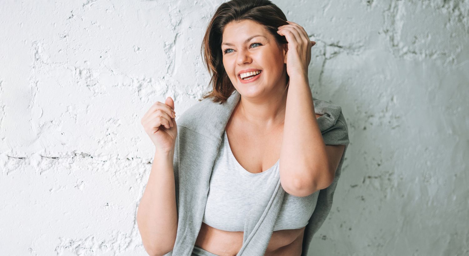 Smiling woman in casual clothing against wall.